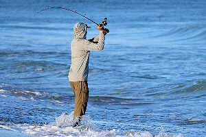 Young surf fisherman angler casting into ocean.